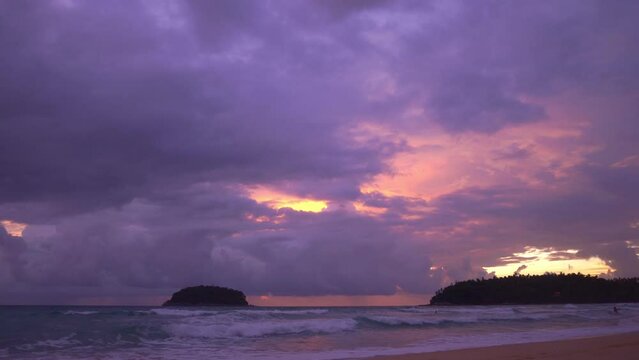 smooth waves hit on the beach at puple sunset..purple clouds cover the ocean during colorful cloud in sunset at Kata beach Phuket..video 4K. Scene of pink light in the sky background..