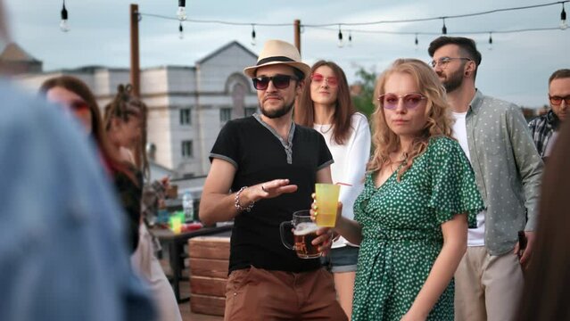 Cheerful friends enjoy summer evening roof party at terrace dancing drinking alcohol