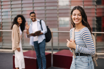 Happy three young interracial university students on break relaxing on campus. Brunette girl wears casual clothes. Relaxation concept