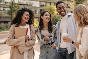 Happy young interracial students chatting with each other after class standing outside. Guy and girls wear casual clothes to study. Lifestyle concept, sincere emotions