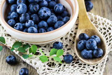 Top view of fresh blueberries in a clay dish with wooden spoon on old wooden background