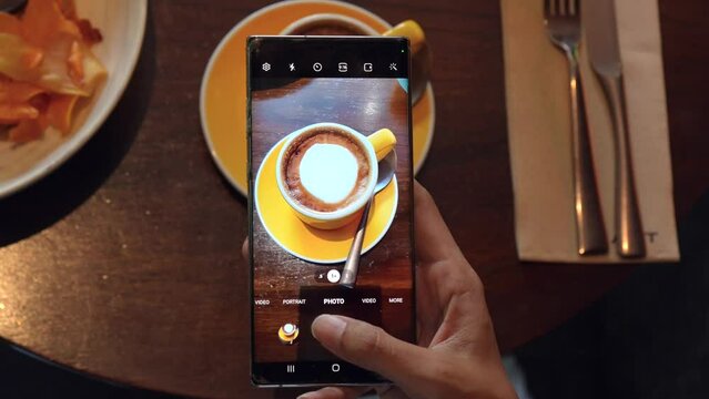 Hand of a woman using a phone to take a picture of coffee