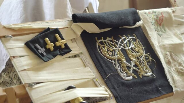 Medieval Embroidery - Old Woman Embroidering Design On Black Fabric With Gold and Silver Thread With Rectangular Frame. - close up