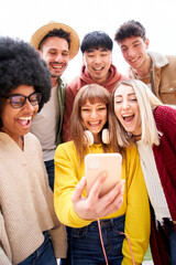 Obraz premium Vertical photo. Multicultural group of friends using cell phones and laughing - Cheerful students lined up and looking at smartphone screen. Young people smiling and looking at their mobile.