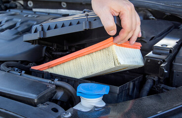 Replacing an old dirty air filter in the engine compartment of a car engine. The mechanic is...