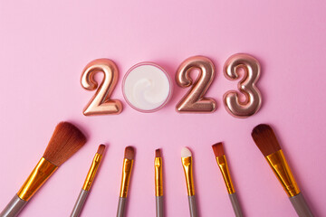 Top view of the makeup brushes on pink background.Rose gold numbers 2023 above.Good for new year...