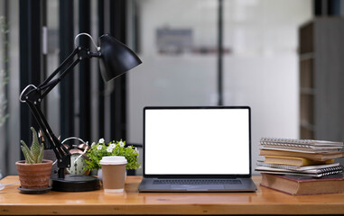Front view computer laptop with empty screen, coffee cup, pencil holder, notebook and house plant on wooden table.