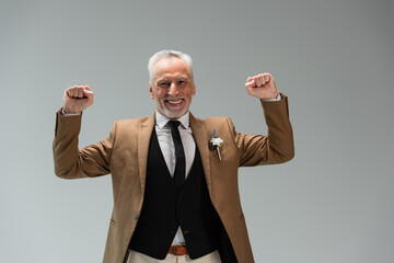 cheerful middle aged groom in suit with floral boutonniere gesturing isolated on grey