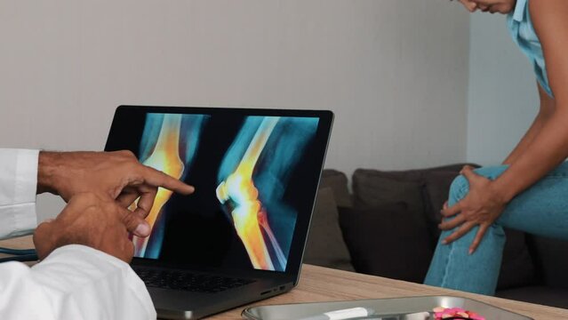 Doctor showing x-ray of pain in the knees on a laptop with woman patient