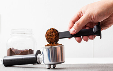 A man pours coffee from a measuring spoon into a coffee maker's horn on a white background. Copy space for text, isolated