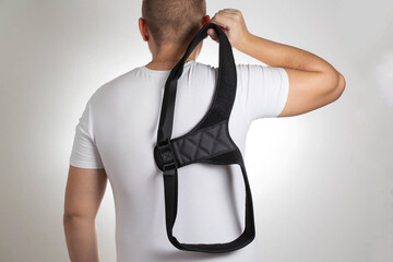 A man in a white T-shirt with a black posture corrector on a white background. Back pain and...