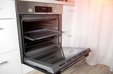 Modern electric oven with telescopic rails and steel baking tray. Hinged oven door. Black oven in a white kitchen.