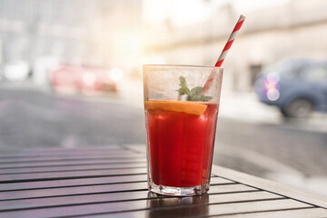 Fresh fruit coctail with drinking straw stands on wooden table of street cafe outdoor