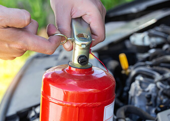 Naklejka premium A man takes out a pin from a car fire extinguisher. The concept of the expiration date of a fire extinguisher, extinguishing a fire. Close-up