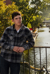 Young man leaning against an iron rail fence with a beautiful river walk in the background.