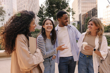 Four young interracial high school students have hilarious conversation taking break from their outdoor activities. Guy and girls wear casual clothes on warm day. Happy day concept