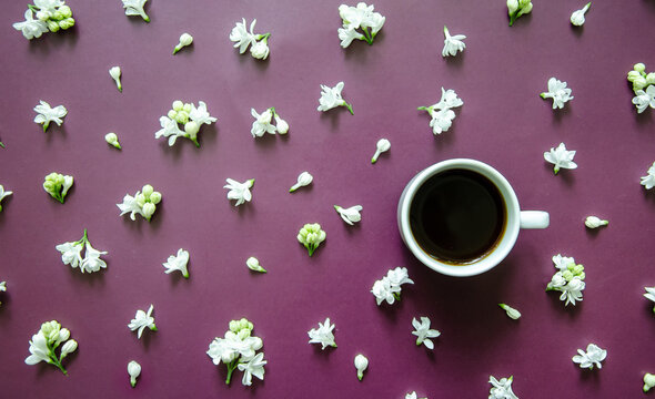 Flatlay dark purple background with small white lilac flowers, white coffee cup on textured background - Powered by Adobe