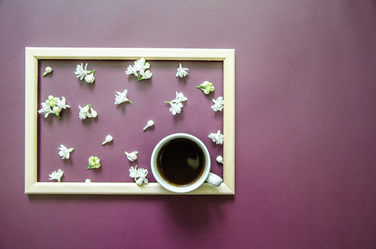 Flatlay dark purple background with small white lilac flowers? white coffee cup on textured background inside a wooden frame - Powered by Adobe