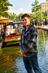 Handsome young man standing by a canal with the sun to his back and a confident expression.