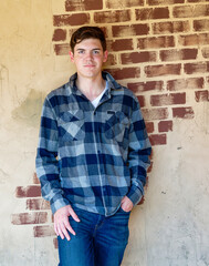 Handsome young man standing in front an old brick wall looking confident and relaxed..
