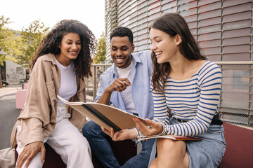 Happy young interracial students with notebooks study homework together outdoors. In spring, guy and girls wear casual clothes. Friendship concept