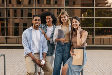 Diverse young classmates walking after class on campus, looking at camera. Guy and girls wear gadgets to study. Concept of enjoying moment