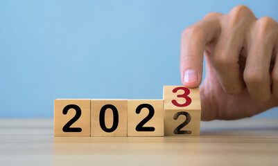 Man hands flipping of 2022 to 2023 on wooden block cube.happy new year 2023.Teble and blue...