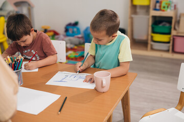kids sitting on desk and drawing in kindergarden