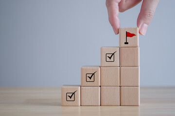 Checklist Survey and assessment. quality Control. Goals achievement and business success. Hand Holding wooden block with red flag icon and check mark on cube ladder.