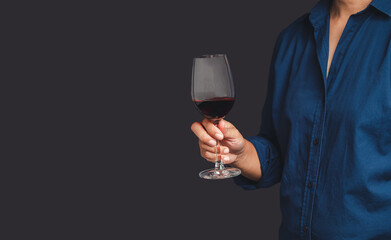 Close-up of hand holding a red wine glass while standing on a gray background