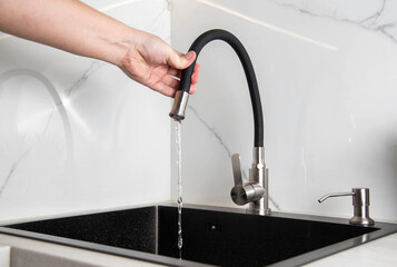 Contemporary kitchen faucet with curved spout set against white porcelain stoneware tiles. Water...