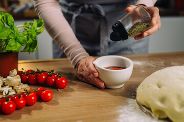 woman adding oregano into tomato dressing for pizza