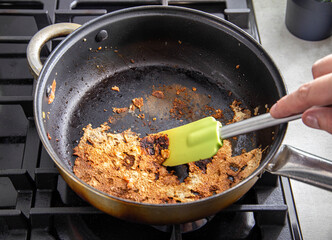 A spatula for stirring food picks off burnt food in a pan. Poor quality Teflon coated pans. Close-up