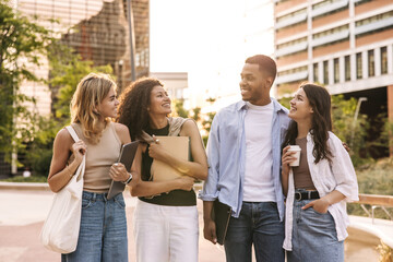 Group of young caucasian, african students walking together to university on warm sunny day. Guy with girls wear casual clothes. Modern lifestyle, people and youth concept