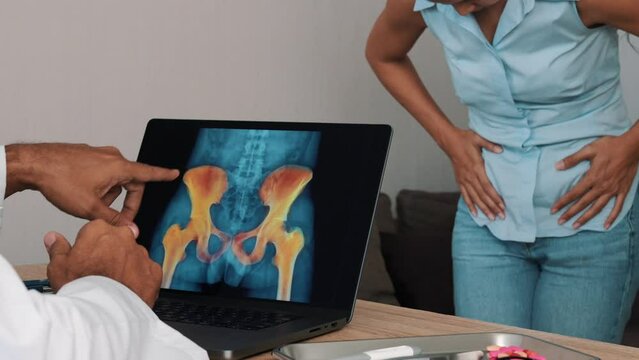 Doctor showing x-ray of pain in the hips on a laptop with woman patient