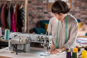 Charismatic dressmaker lady at her tailoring atelier using the sew machine happy and concentrated...
