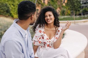 Positive young african friends chat spending time outdoors during day. Brunette girl and guy are wearing summer clothes. Modern lifestyle, people and youth concept