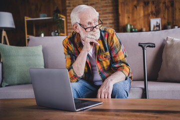 Photo of thoughtful clever man pensioner wear checkered shirt writing modern gadget sitting sofa...