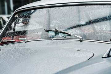 Raindrops on the windshield and working wipers of a retro car. Cinematic and atmospheric mood of the picture - obrazy, fototapety, plakaty