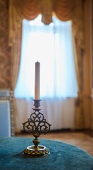 The candle stands on the table in an old bronze candlestick.