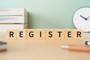 登録のイメージ｜「REGISTER」と書かれたブロックが置かれたデスク
