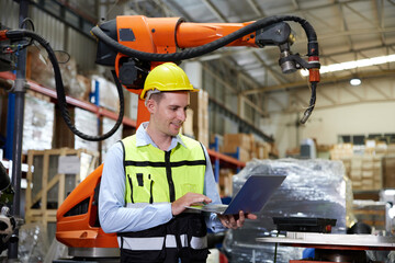 factory worker or engineer holding a laptop computer and controlling robot machine in the factory