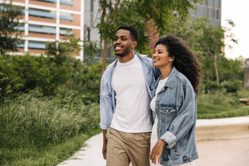Happy african young friends spend weekend walking in spring city. Brunette guy and girl wear casual clothes. Relaxed lifestyle, concept