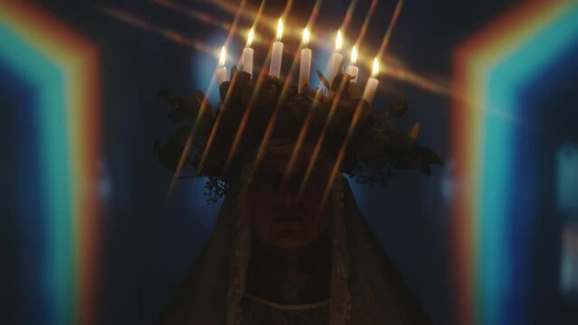 Portrait of queer man with candle lit wreath and veil posing for camera in dark studio with blinking light and kaleidoscopic projection in background