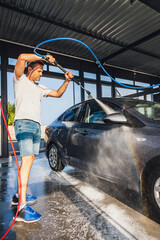 A man washes his car at a self-service car wash using a hose with pressurized water
