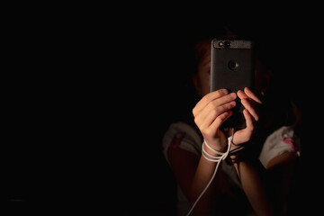 Mobile addiction and digital dependence concept. POrtrait of young girl tied with cell phone charger cord and holds smartphone. Copy space for design. Horizontal image.