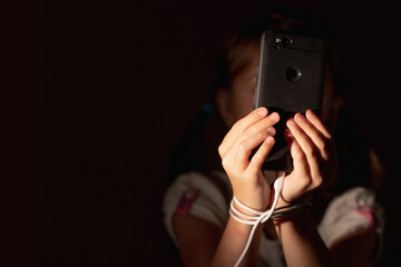 Mobile addiction and digital dependence concept. POrtrait of young girl tied with cell phone charger cord and holds smartphone. Copy space. Horizontal image.