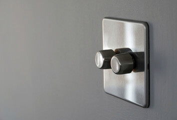 An energy saving stainless steel double dimmer light switch on a grey internal wall of a home. 
