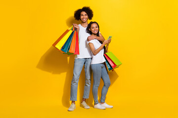 Fototapeta premium Full length photo of two positive partners cuddle hold telephone packages isolated on yellow color background