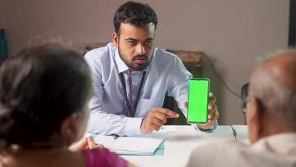 Happy banker explaining online banking from green screen mobile phone to customers at bank - concept of advertisement, app promotion and financial service.